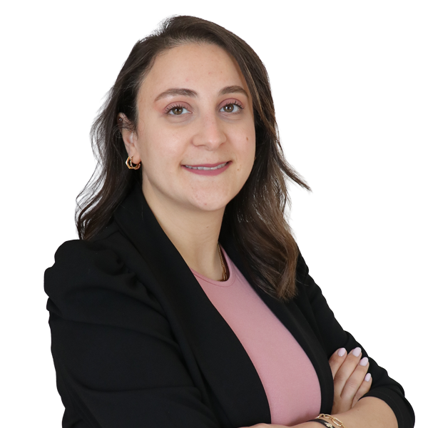 Portrait of a woman with brown hair wearing a black blazer and pink top, arms crossed, smiling against a light wall—professional headshot.