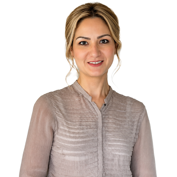 Professional headshot of a smiling blonde woman in a beige blouse standing in an office setting, facing the camera.