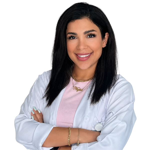 Smiling female medical professional with dark hair in a white lab coat over a pink top, arms crossed.